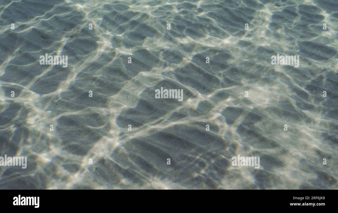 Glare of sun plays on sandy bottom in shallow water. Top view on sandy seabed in shallow water with diagonal lines of sand and sun glare on its surfac Stock Photo