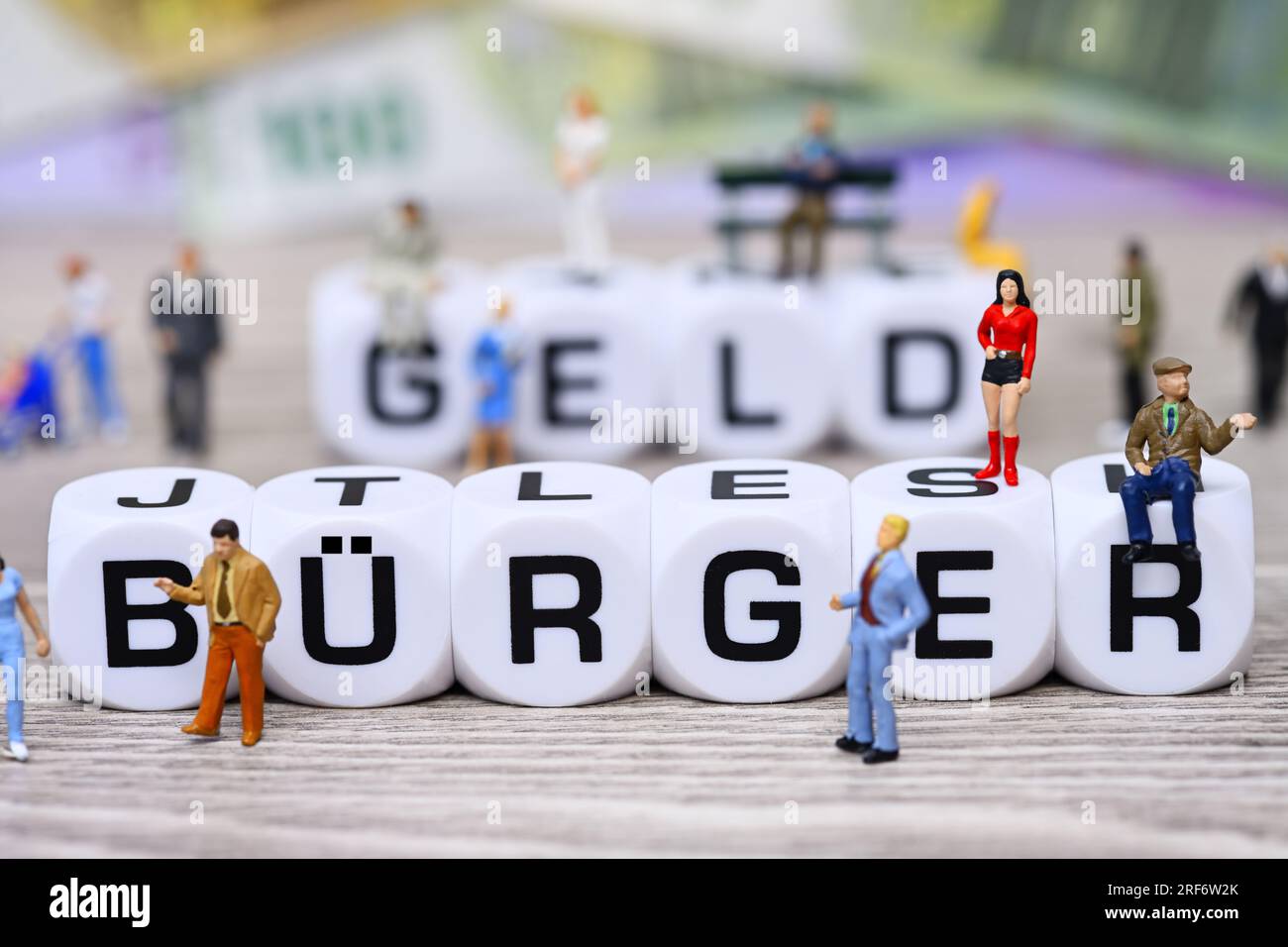 Würfelbuchstaben formen den Schriftzug Bürgergeld umgeben von Miniaturfiguren Stock Photo
