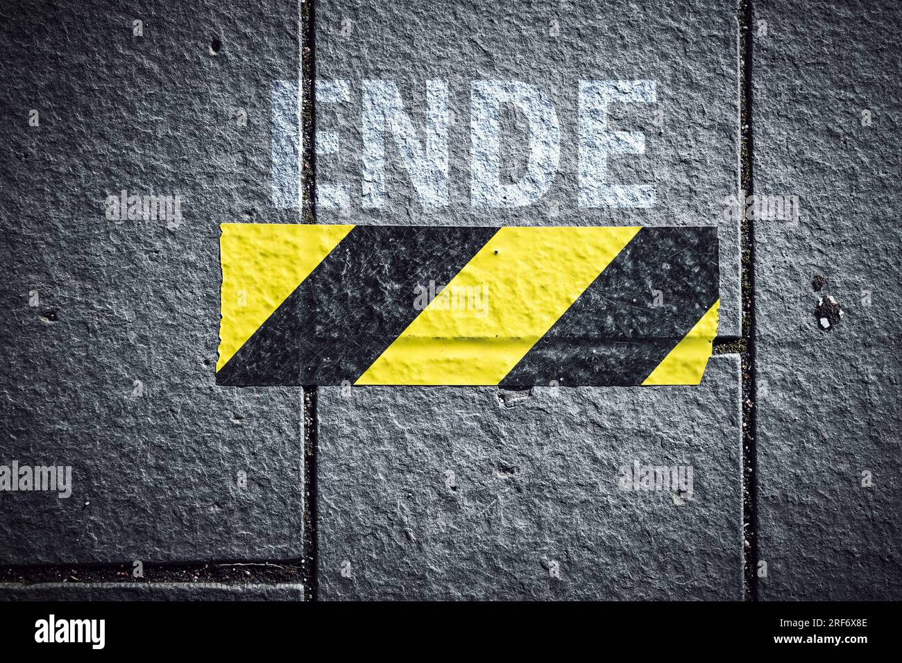 FOTOMONTAGE, Der Rest eines gelb-schwarzen Absperrbandes auf einem Weg mit dem Schriftzug Ende, Symbolfoto für das Ende der Corona-Pandemie-Schutzmaßn Stock Photo