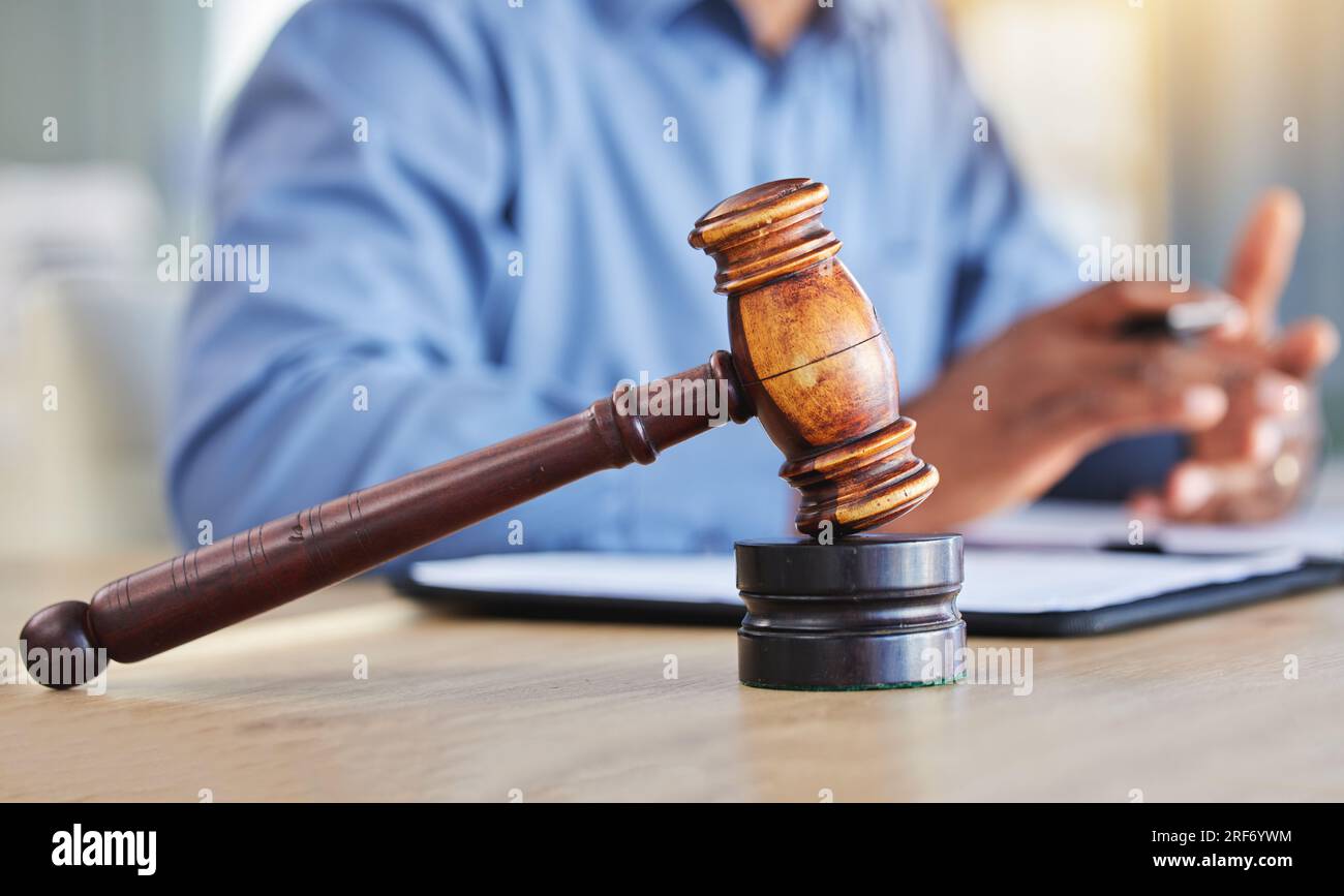 Closeup, lawyer and gavel of judge in office of trial, attention and meeting for justice in courtroom, law firm or table. Hammer, legal tool or Stock Photo