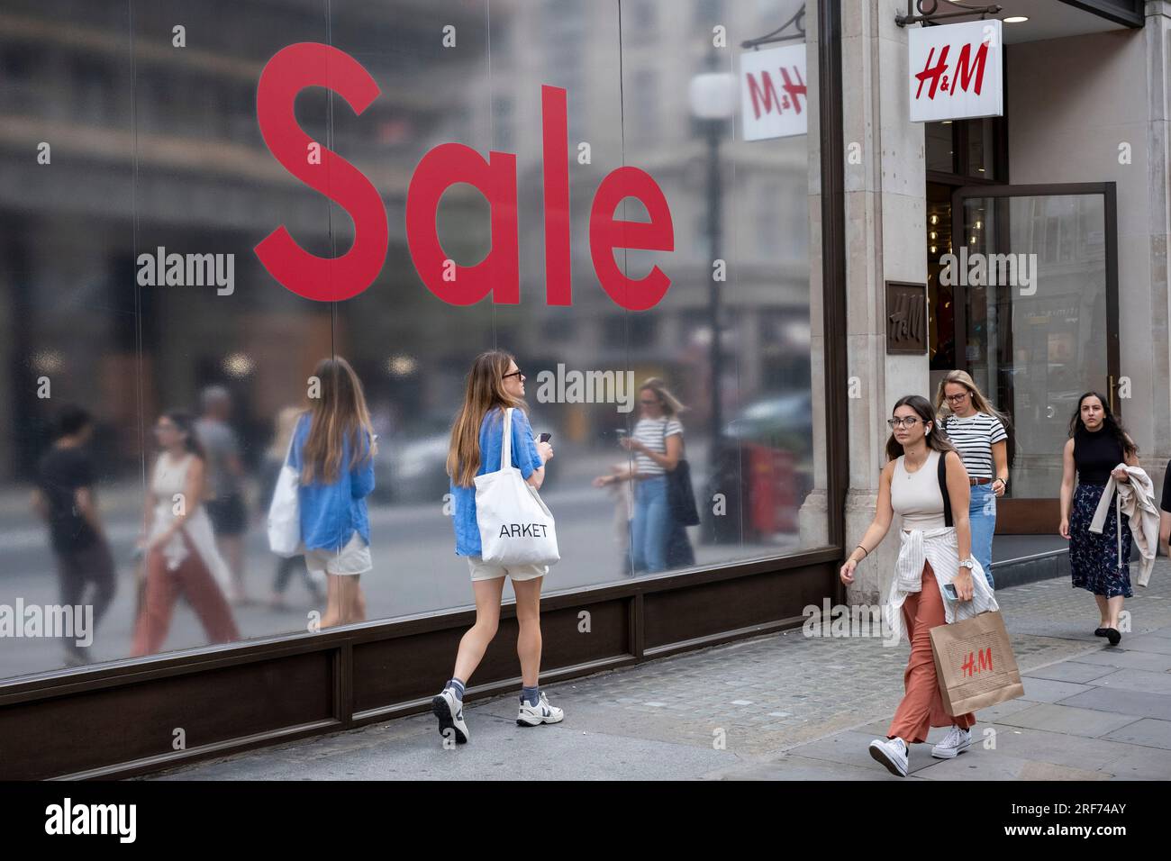People out shopping walk past a large scale sale sign in red and