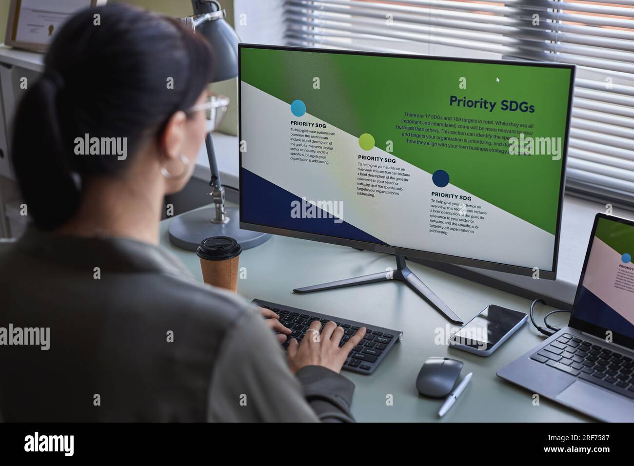 Back view at young woman using computer at desk while working on development strategies Stock Photo