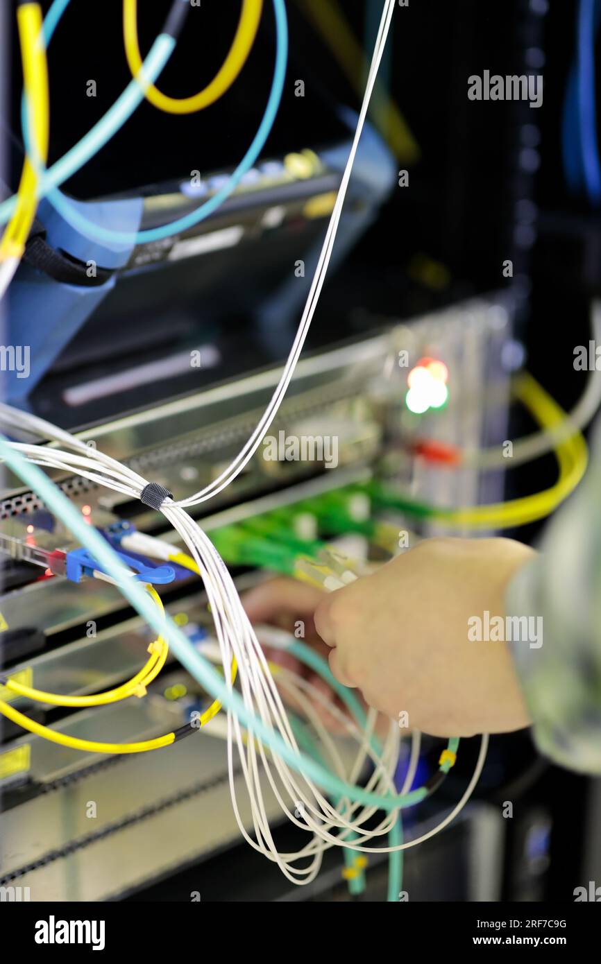hands of engineer plug in fiber optic cables into rack mounted switch Stock Photo