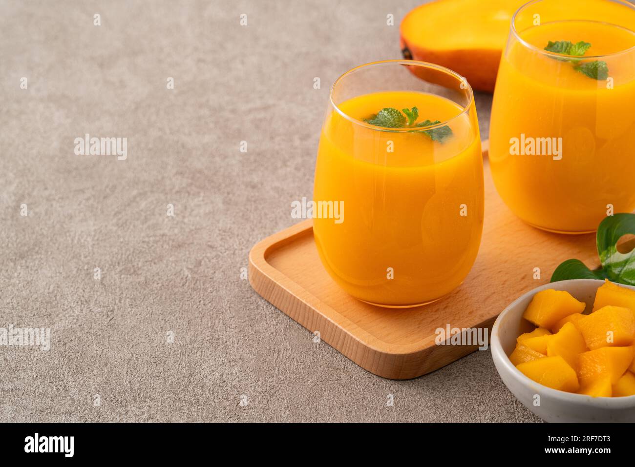 Fresh beautiful delicious mango juice. Close up design concept of smoothie cold drink in glass cup with glass straw on gray table background. Stock Photo