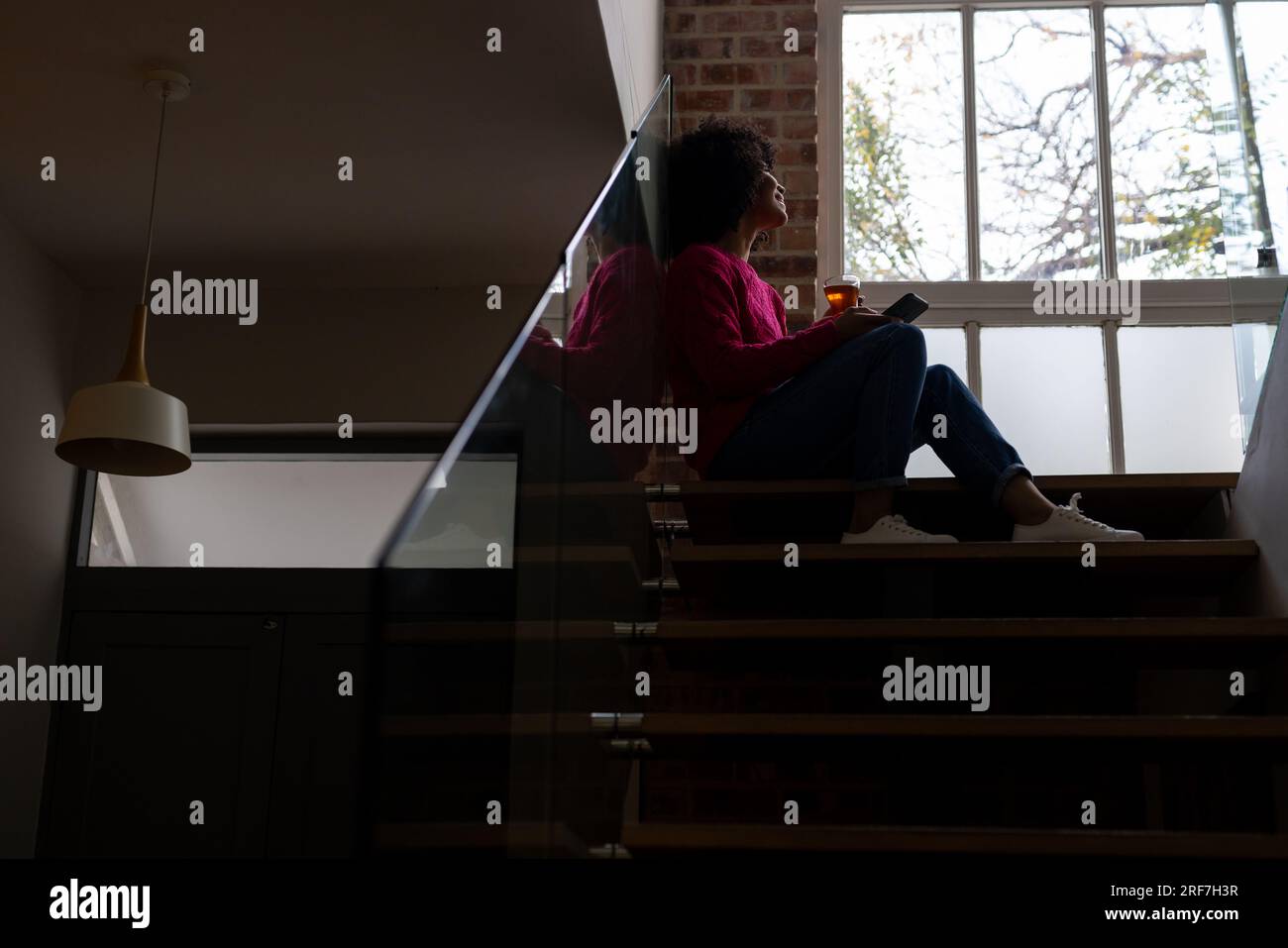 Biracial woman drinking tea and using smartphone at home, copy space Stock Photo