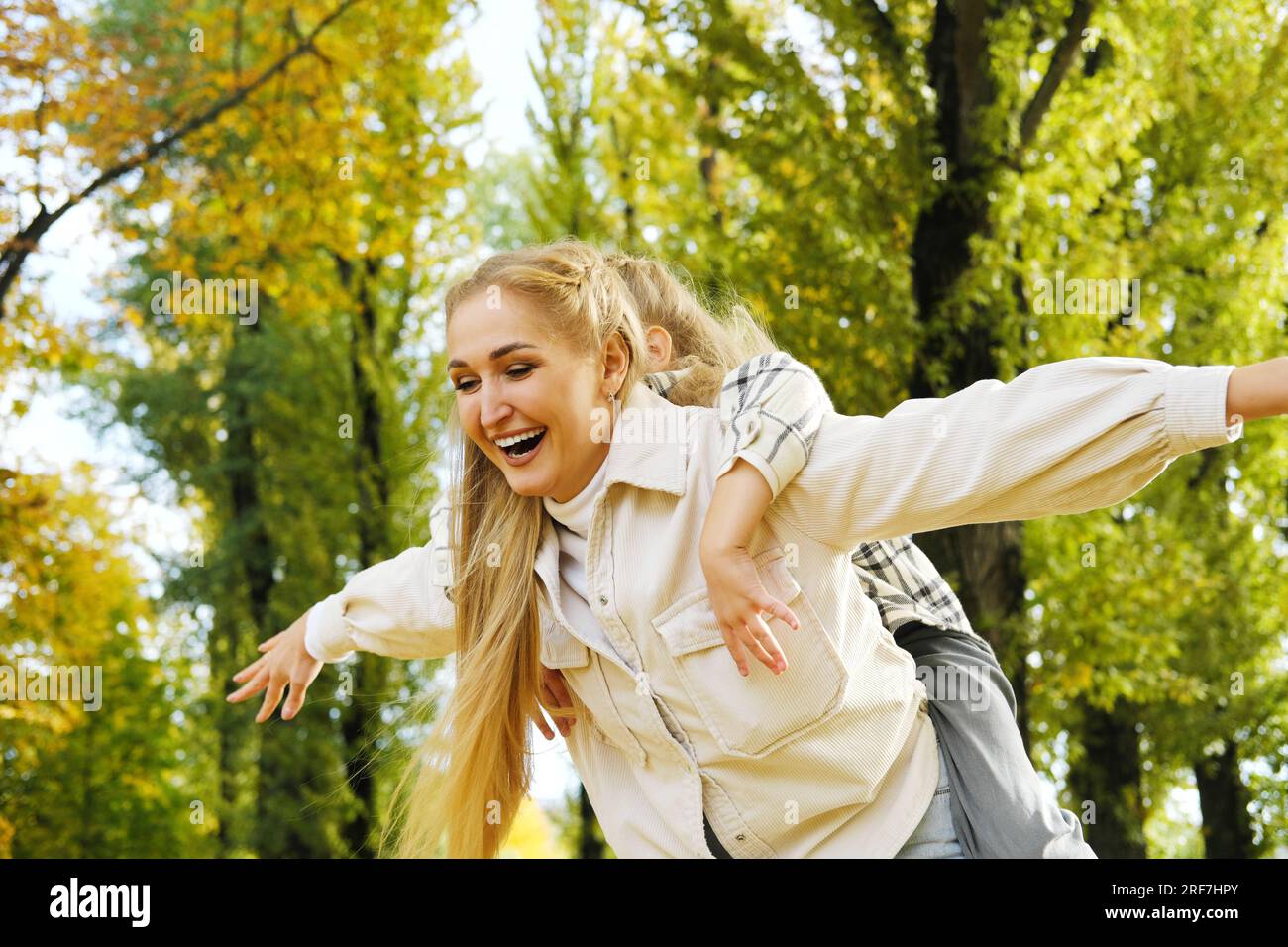 Play, flying or mother with girl on back in autumn park bonding, quality time and playing outdoors. Love, airplane and happy mom piggyback with child Stock Photo