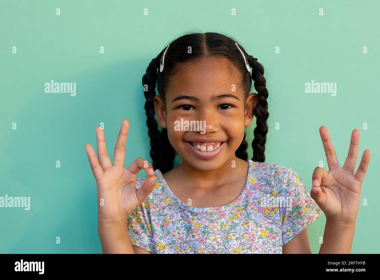 Biracial schoolgirl doing sign language gestures over blue background at elementary school Stock Photo