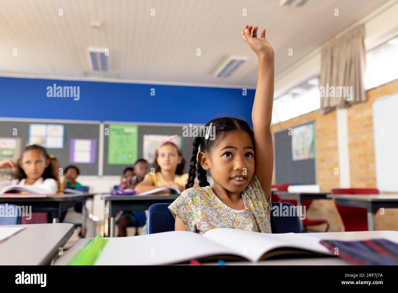Happy biracial school girl raising her hand in classroom at elementary ...