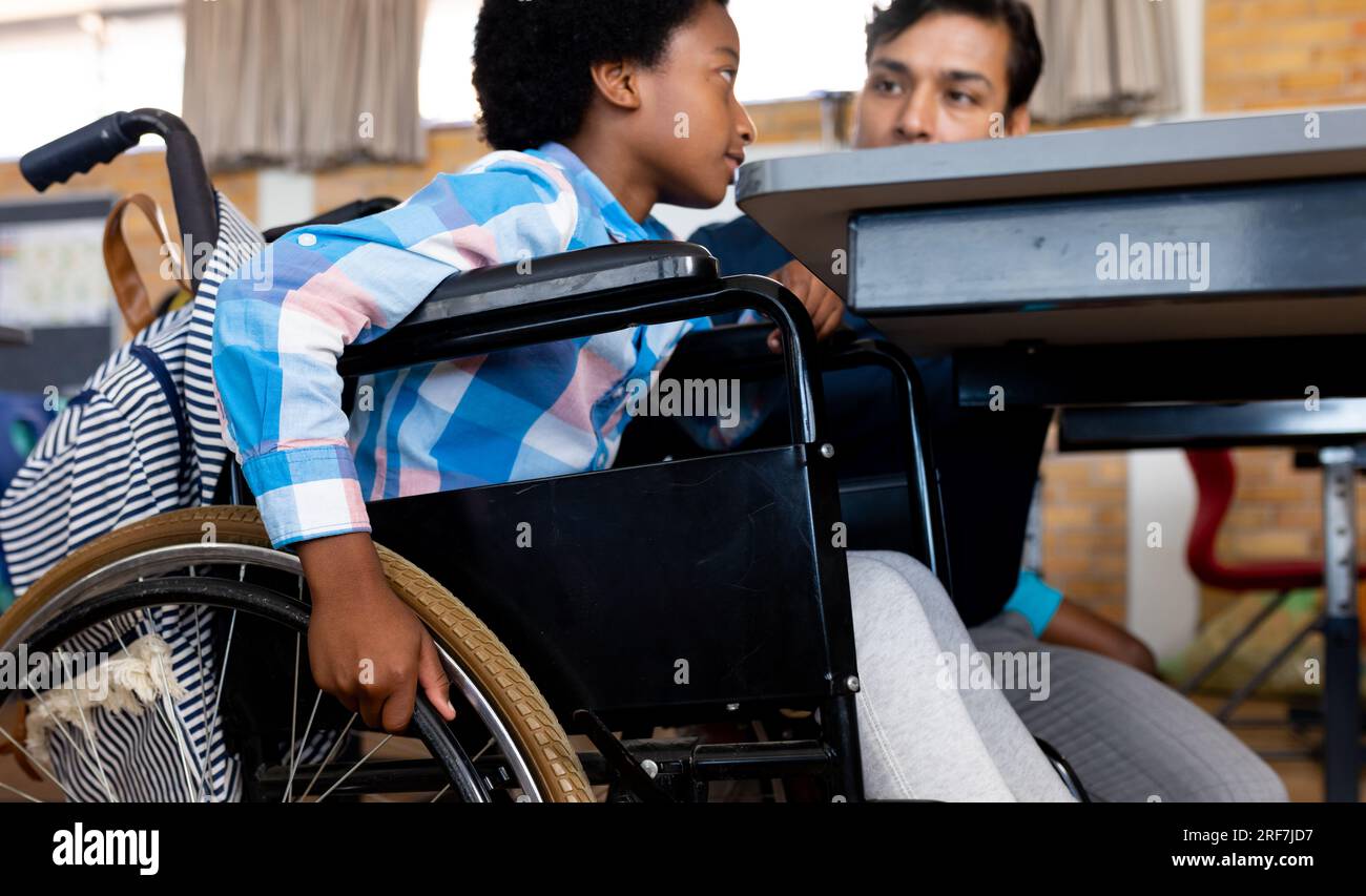 Diverse boy in wheelchair and male teacher in elementary school classroom Stock Photo