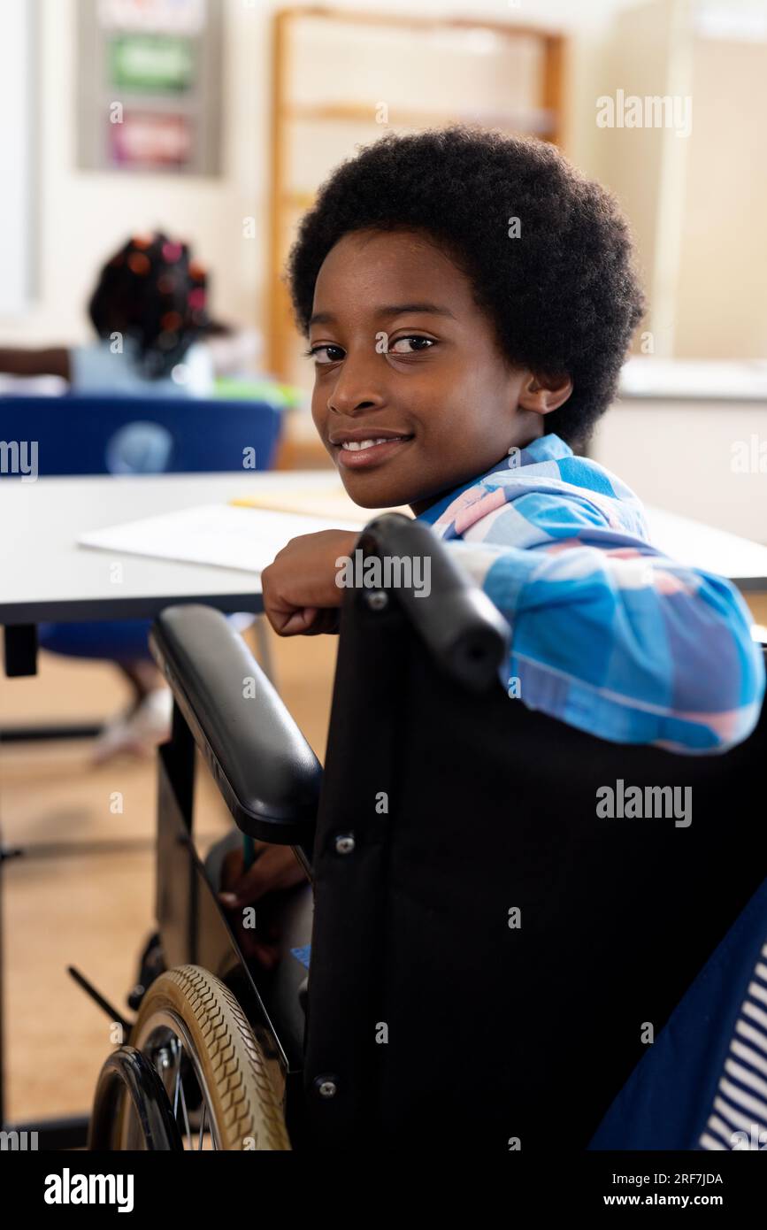 Portrait of happy biracial boy in wheelchair smiling in class at elementary school Stock Photo