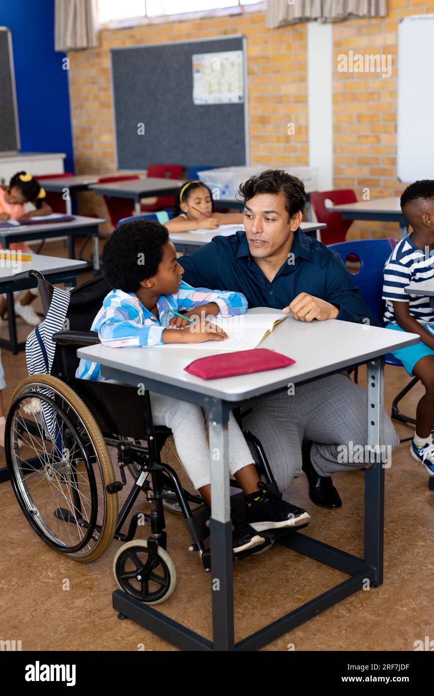Biracial male teacher with boy in wheelchair in class at elementary school Stock Photo