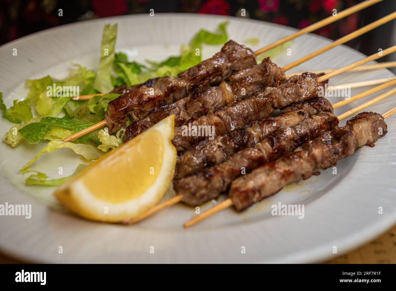Grilled lamb skewers with lemon on a white plate in an Italian