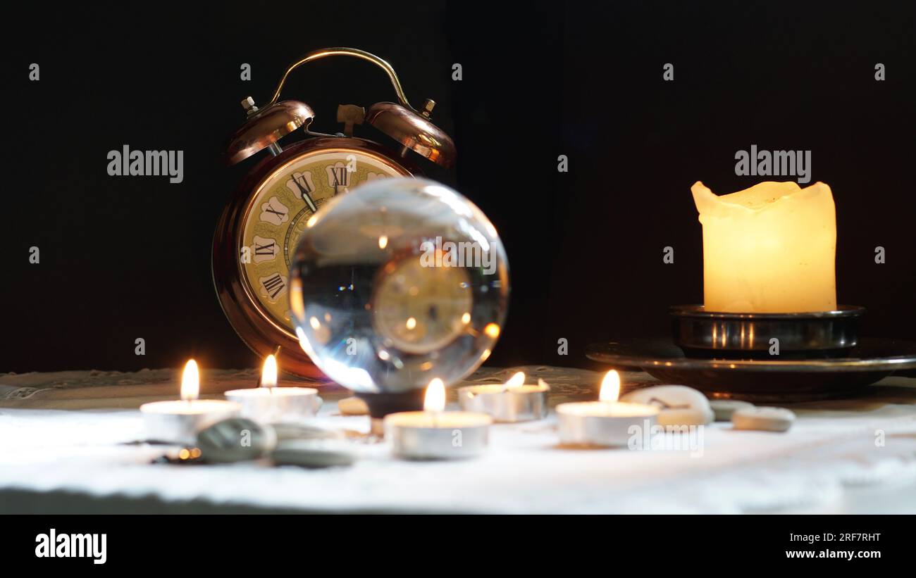 A gold colored clock showing the eleventh hour. A crystal ball, candles. What does the future bring? Time is running out concept. Stock Photo