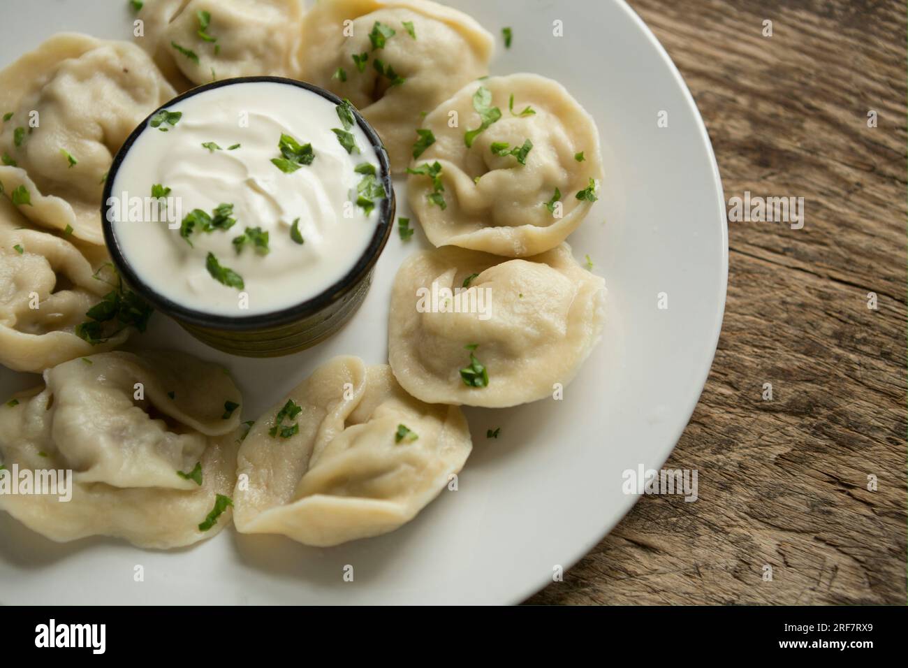 Homemade Russian dumplings, or Pelmeni, that have been stuffed with minced pork and onion before being boiled and served with soured cream. Garnished Stock Photo