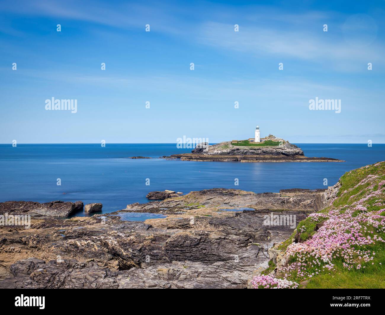 18 May 2023: Godrevy Head, Cornwall, UK - Godrevy Head and Godrevy Lighthouse on a sunny spring day, and sea thrift in bloom, long exposure. Stock Photo