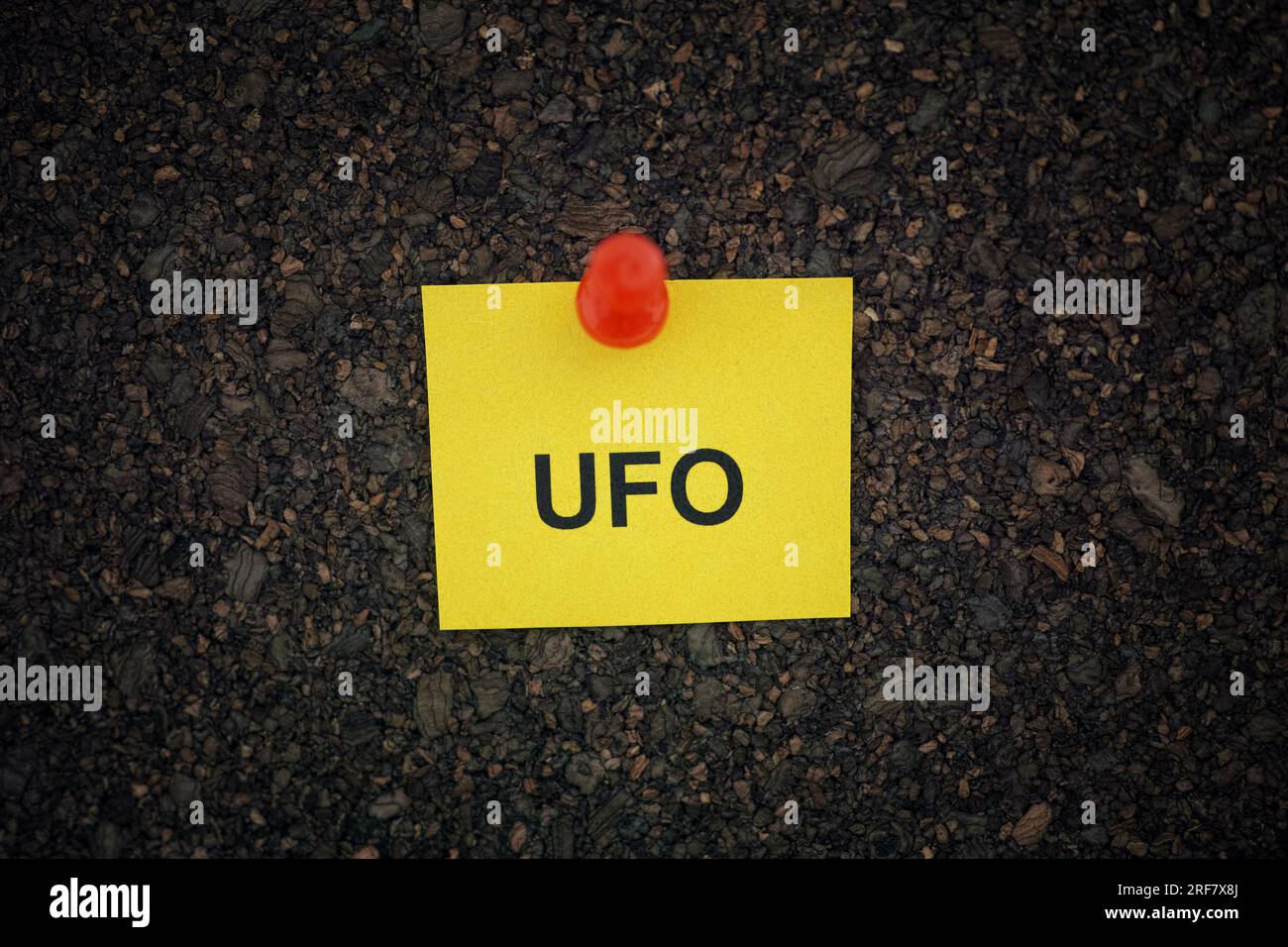 A yellow paper note with the abbreviation UFO on it pinned to a cork board. Close up. Stock Photo