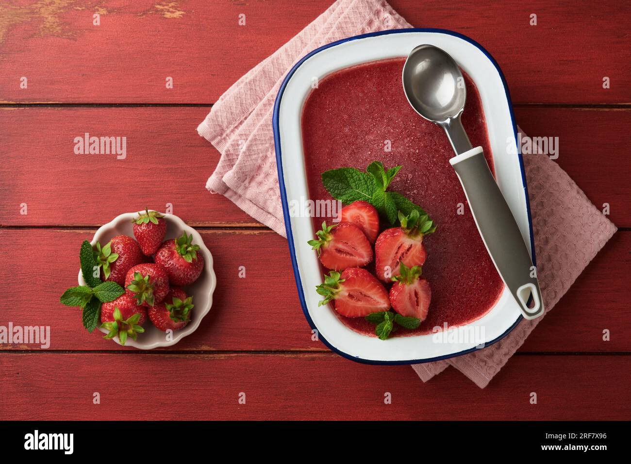 Strawberry granita or fresh berry sorbet in white rustic bowl on old wooden table background. Ice cream with strawberry and mint. Summer treat. Top vi Stock Photo