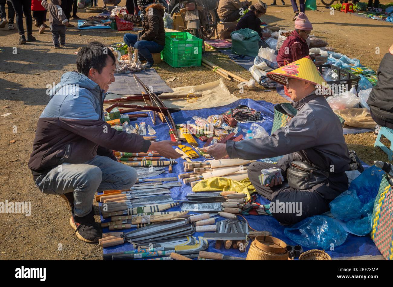 A White Thai ethnic minority man buys a handmade knife at a knife stall in a busty open-air market in Mai Chau, Vietnam. Stock Photo