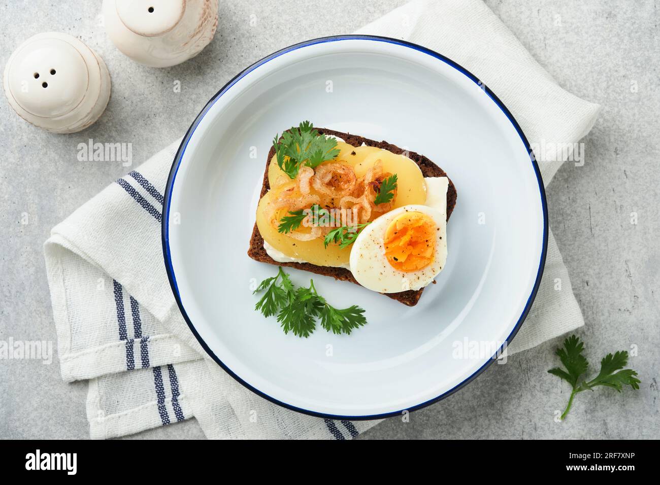 Open sandwich or smorrebrod with rye bread, herring, eggs, caramelized onions, parsley and cottage cheese on old wooden rustic table backgrounds. Dani Stock Photo