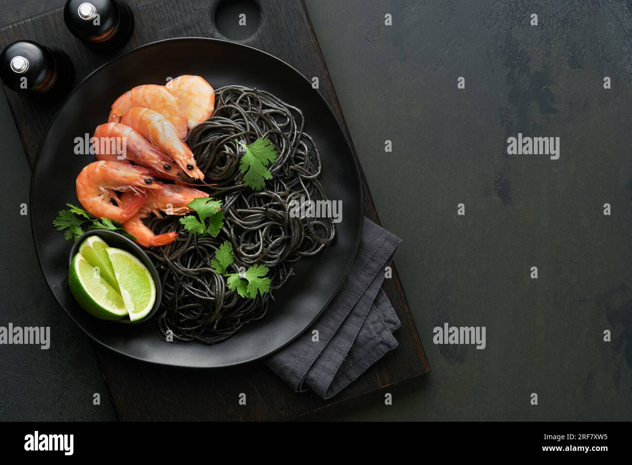 Black spaghetti pasta shrimp on black plate on dark concrete table background. Squid ink pasta with prawns. Pasta seafood. Top view on black stone tab Stock Photo