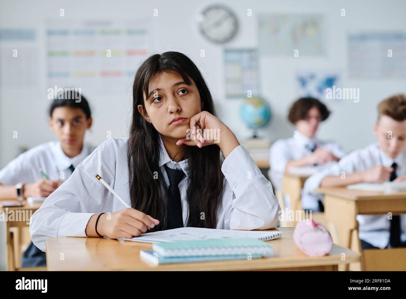 Schoolgirl sitting at her desk and listening to teacher during lesson ...