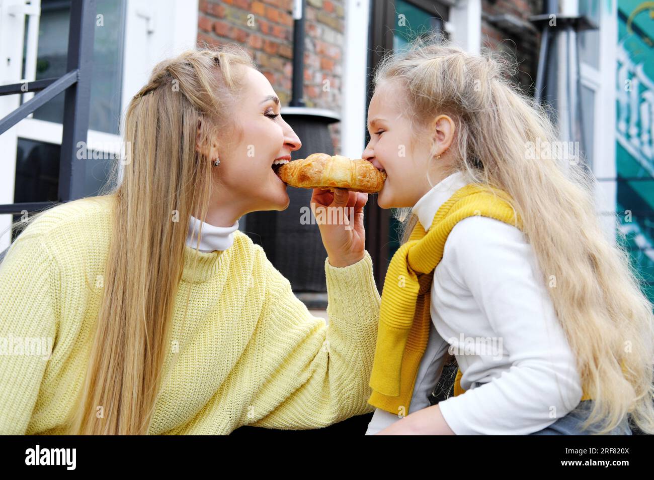 Mom and daughter are sitting on the steps with glasses of hot chocolate and croissants. The family spends the weekend together. mother and daughter on Stock Photo