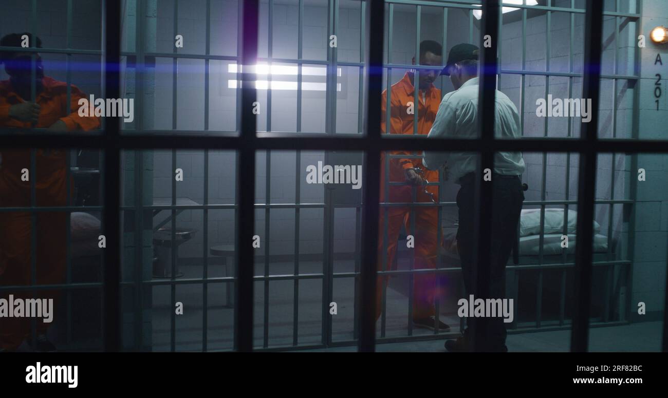 Warden brings guilty prisoner in jail cell and takes off handcuffs. African American man serves imprisonment term in correctional facility or detention center. Murderer in prison cell. Stock Photo