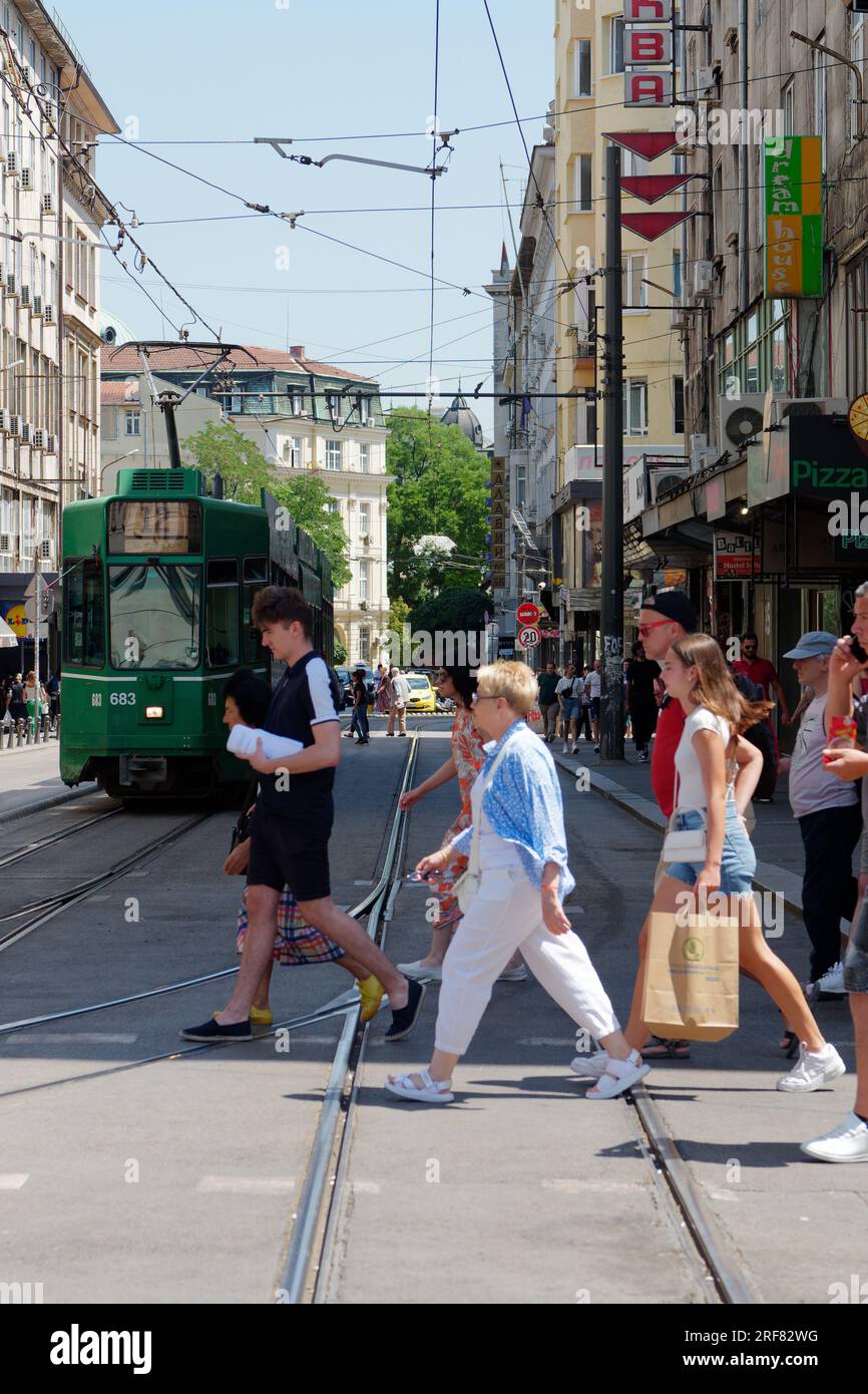 People cross the road in front of a Green Tram aka Streetcar aka Trolley on a street in the City of Sofia, Bulgaria. August 01, 2023. Stock Photo