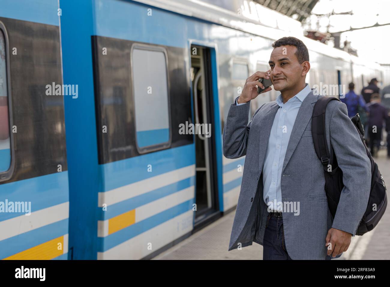 Latin man in a suit waiting for the train and talking on the mobile phone. Stock Photo