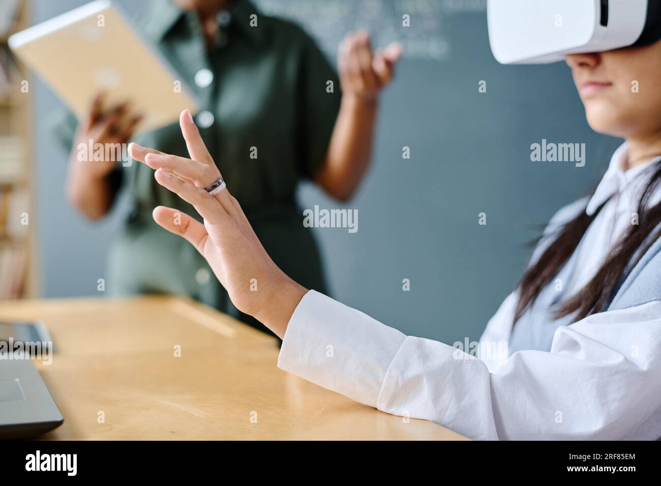 Student using VR glasses at lesson with teacher explaining information in background Stock Photo