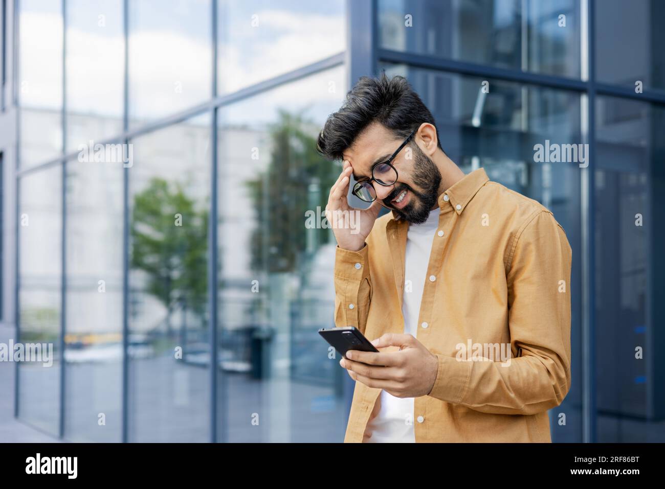 Upset businessman received message with bad news, hispanic man outside office alarm clock cheated and bankrupt, man unhappy with achievement results w Stock Photo