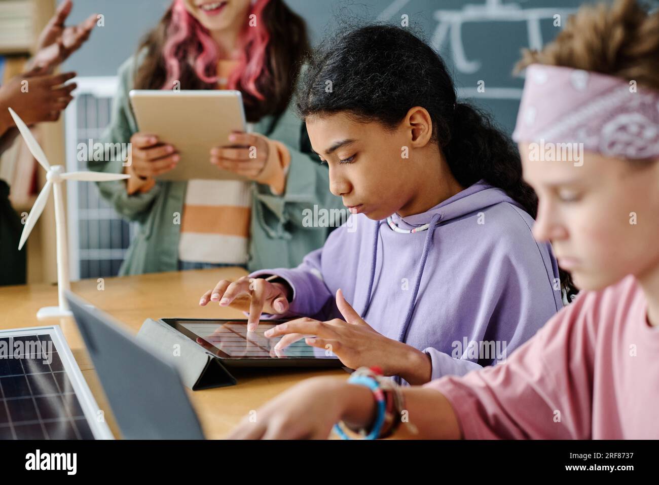 Schoolgirl using gadgets during lesson together with her classmates Stock Photo