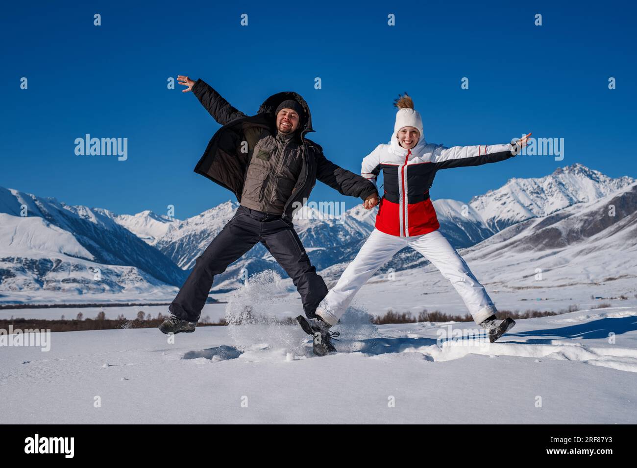 Young happy man and woman jumping on mountains background in winter season Stock Photo
