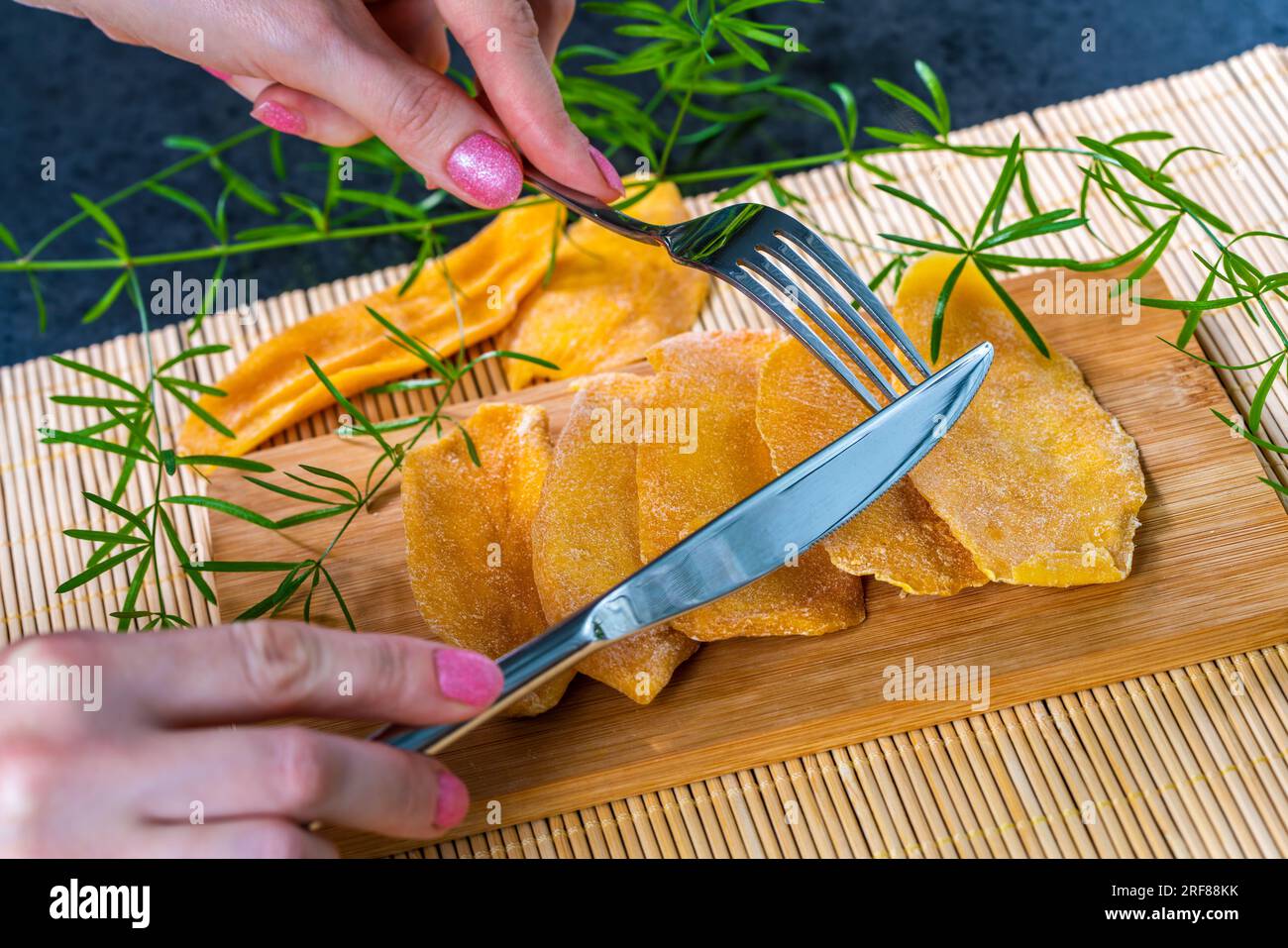 Kitchen table with dried mango on board, woman holding fork and knife Stock Photo