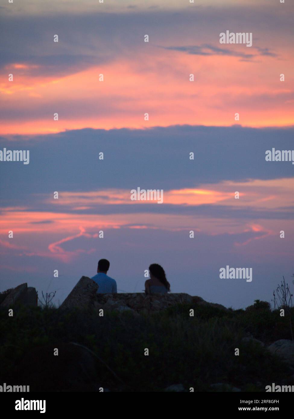 A boy and a girl watch the Sunrise from Cabo de Caballería in Menorca.  .Un chico y una chica observan la fuesta de Sol desde el cabo de Caballería. Stock Photo
