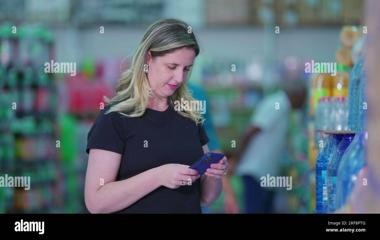 Woman Checking Grocery List on Phone while Browsing Soda Aisle. Candid ...