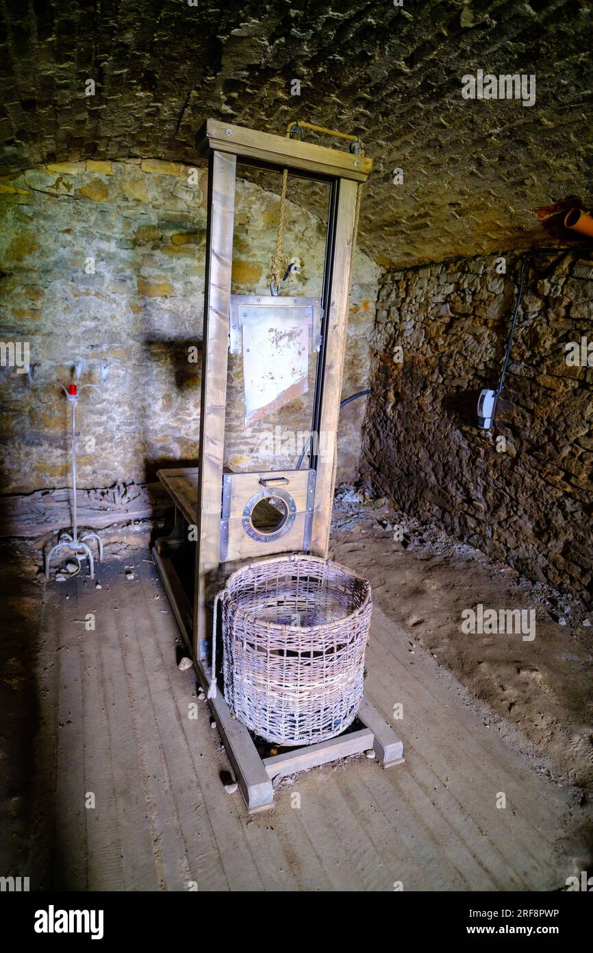 There is little light in the dark basement room. The guillotine, a medieval tool of punishment, stands with a basket made of wicker. Stock Photo