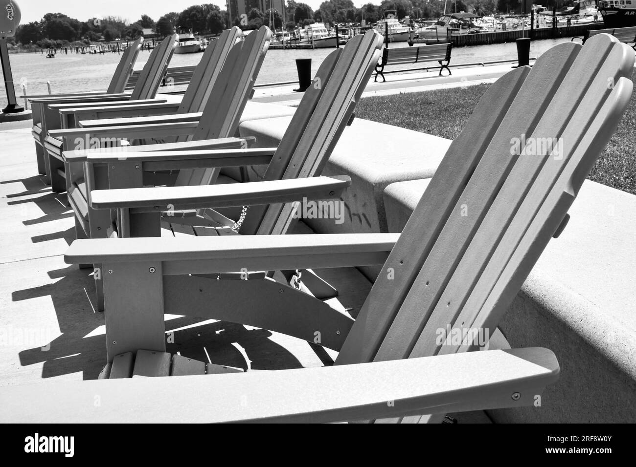 Row of empty Adirondack chairs by the harbor shore Stock Photo