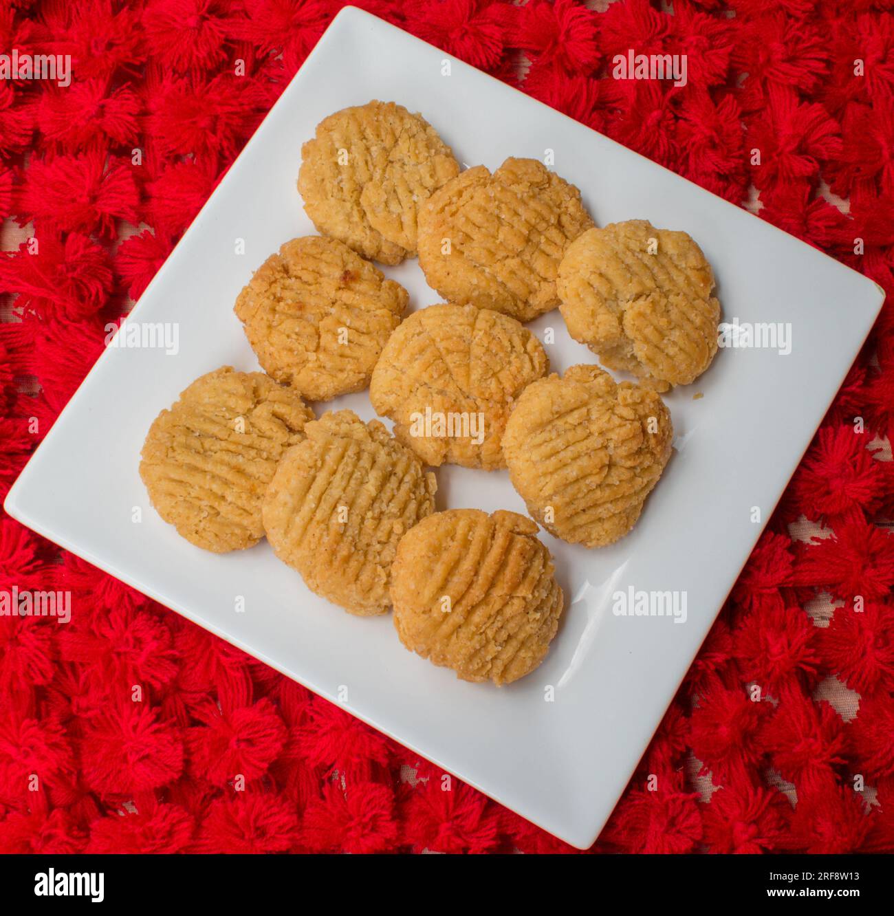 Thekua , an Indian sweet dish snacks in white plate . woman hand putting thekua on plate. Popular in bihar jharkhand. Prashad in chhath festival Stock Photo