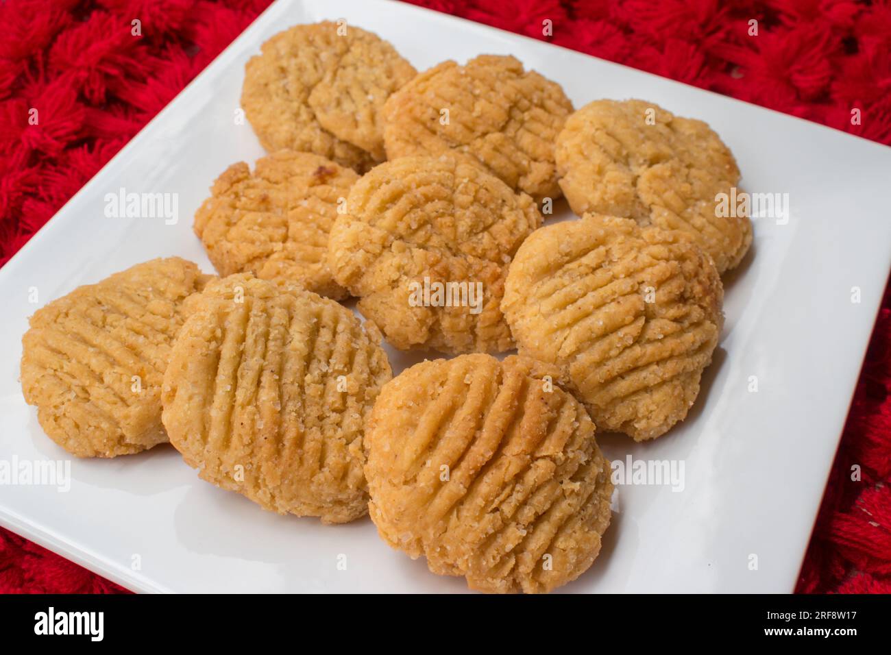 Thekua , an Indian sweet dish snacks in white plate . woman hand putting thekua on plate. Popular in bihar jharkhand. Prashad in chhath festival Stock Photo