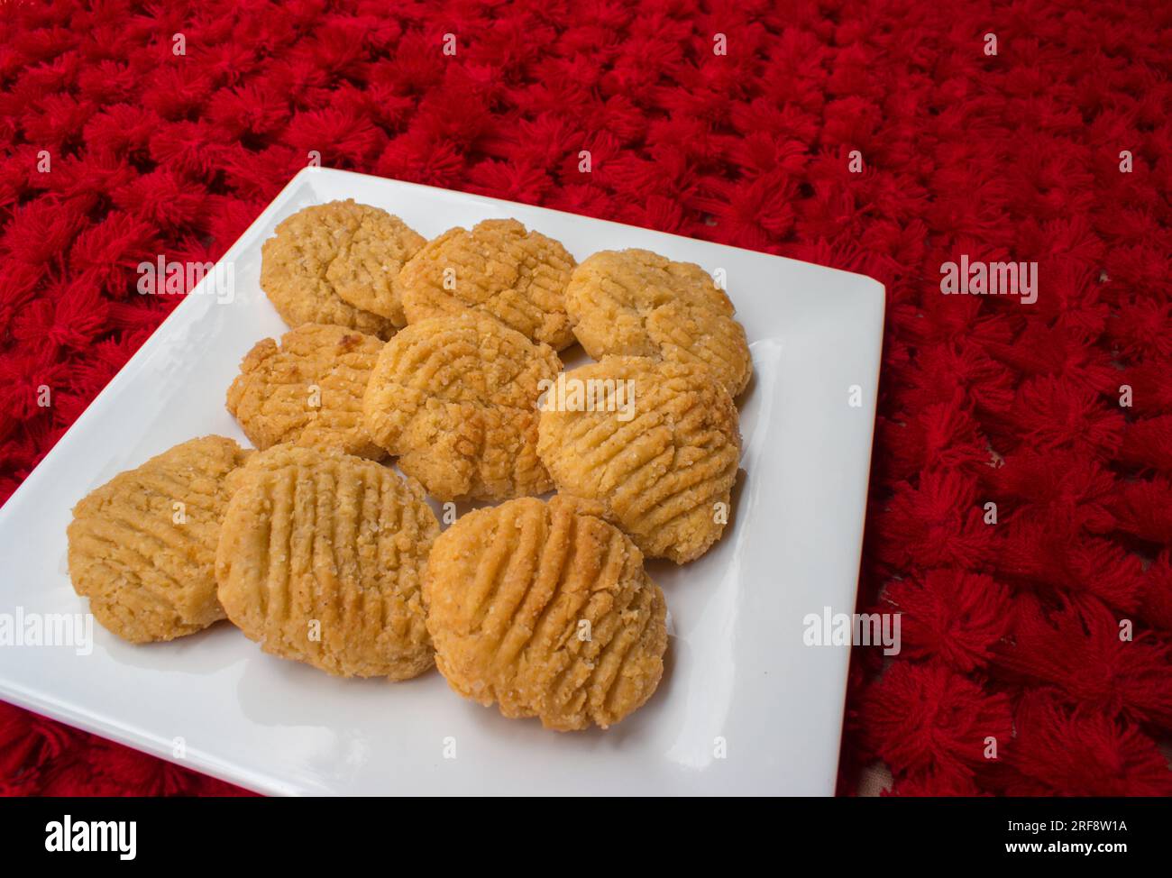 Thekua , an Indian sweet dish snacks in white plate . woman hand putting thekua on plate. Popular in bihar jharkhand. Prashad in chhath festival Stock Photo