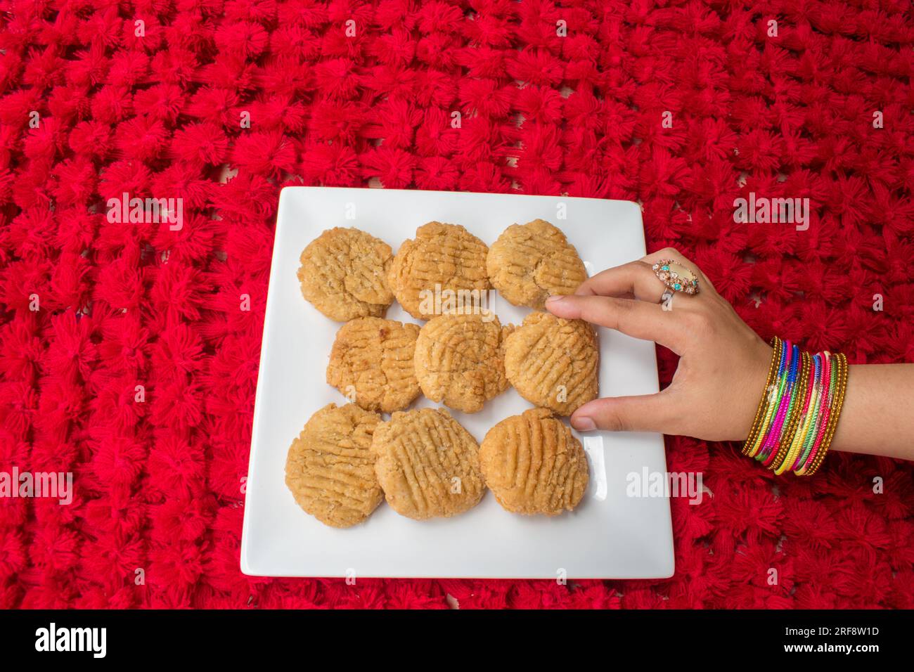 Thekua , an Indian sweet dish snacks in white plate . woman hand putting thekua on plate. Popular in bihar jharkhand. Prashad in chhath festival Stock Photo