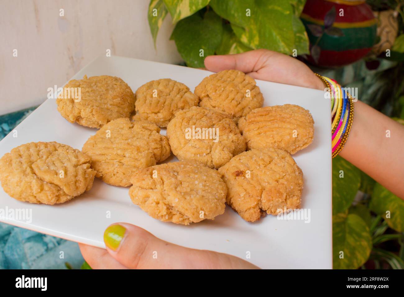 Thekua , an Indian sweet dish snacks in white plate . woman hand putting thekua on plate. Popular in bihar jharkhand. Prashad in chhath festival Stock Photo