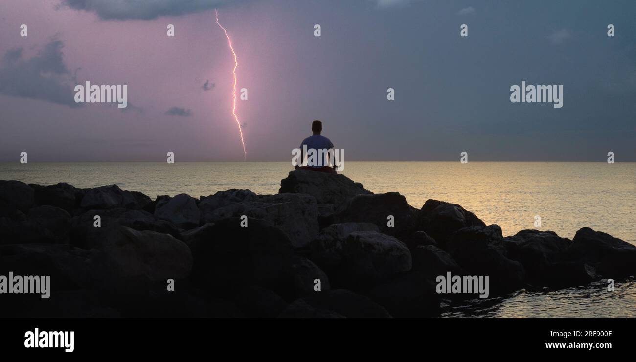 Night sea view with lightning bolt and man practicing yoga on rocks