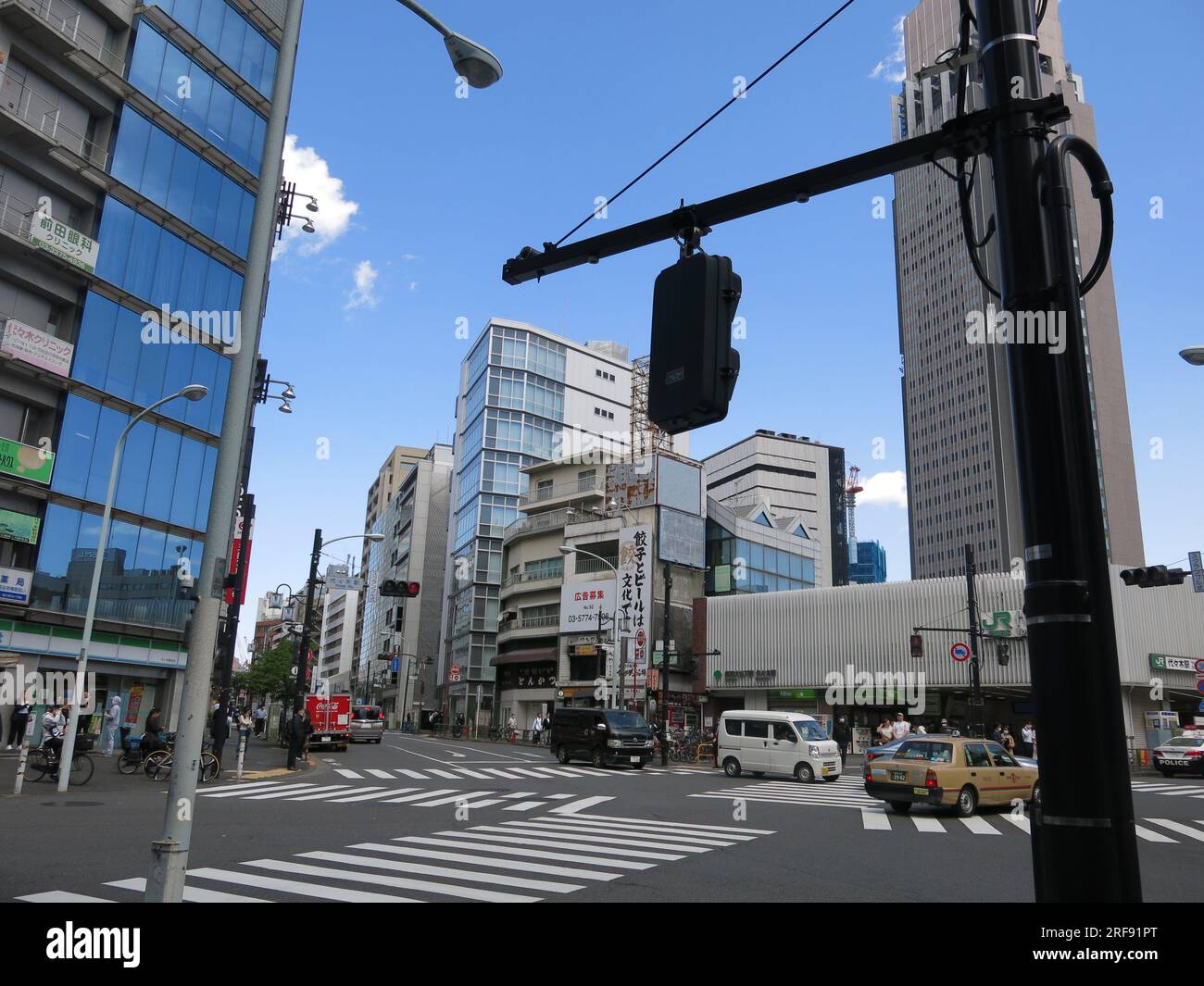 Street scene in Yoyogi, a suburb of wider Tokyo, showing a commercial district with tall buildings, pedestrian crossings & power lines across the road. Stock Photo