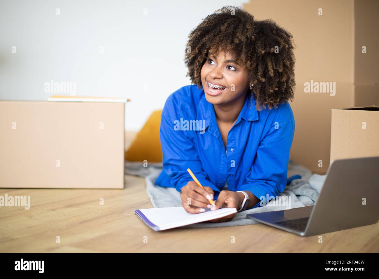 Excited Black Woman With Notepad Relaxing Among Cardboard Boxes In New ...