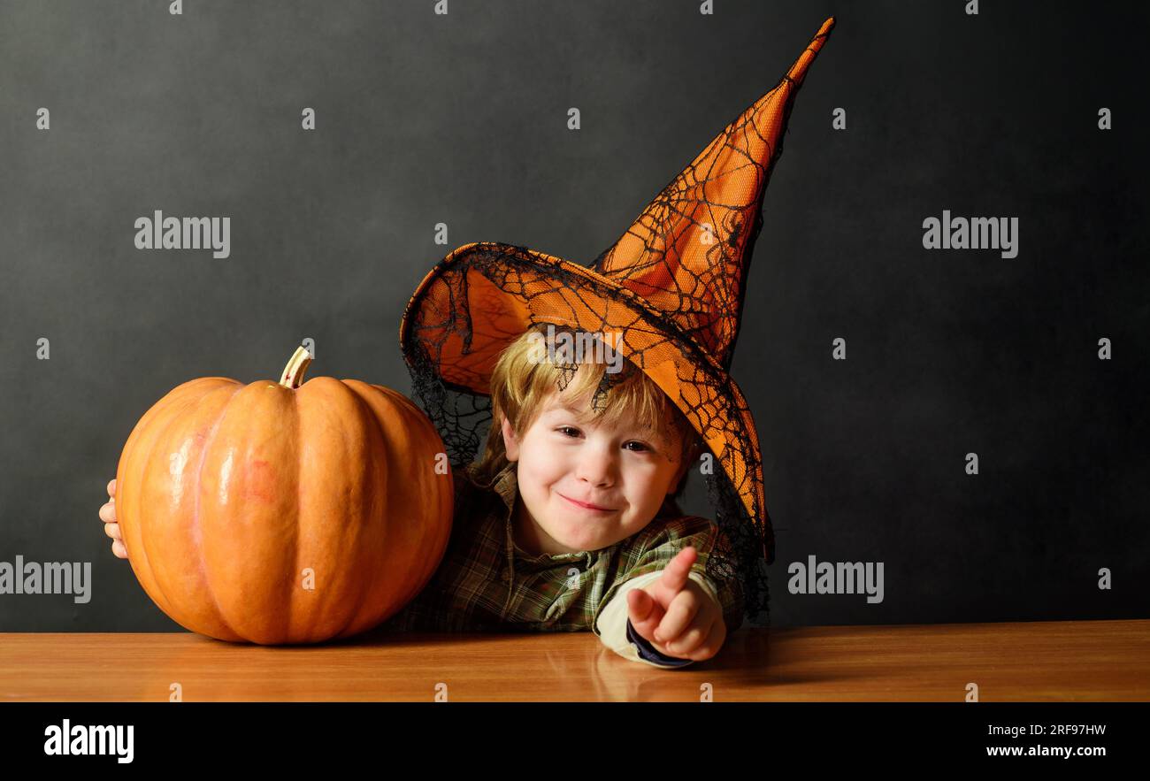 Cute boy in witch hat with Halloween jack-o-lantern. Smiling child in witch hat with Halloween pumpkin. Trick or treat. Preparation for Halloween Stock Photo
