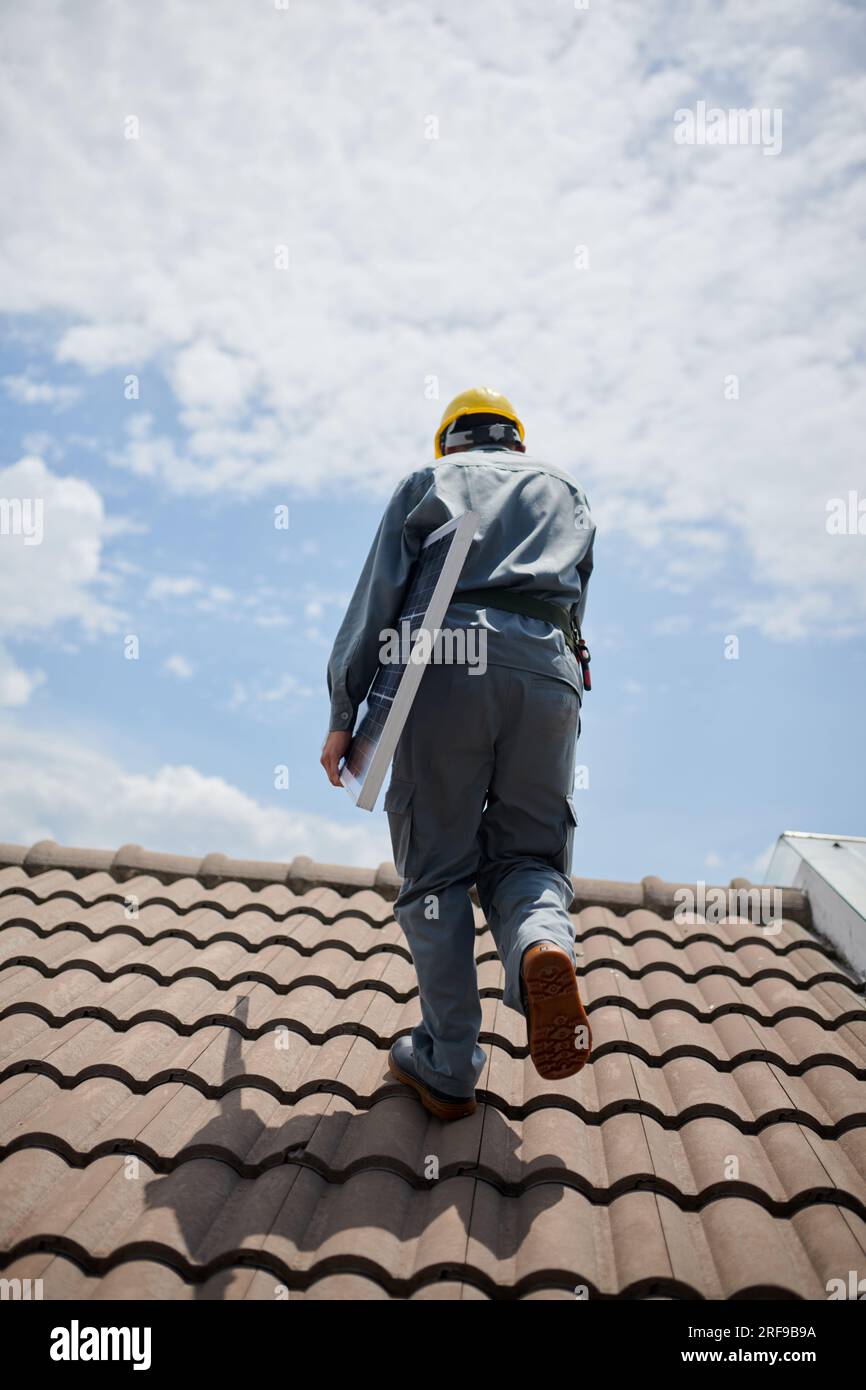 Engineer carrying solar panel when walking on roof, view from back Stock Photo