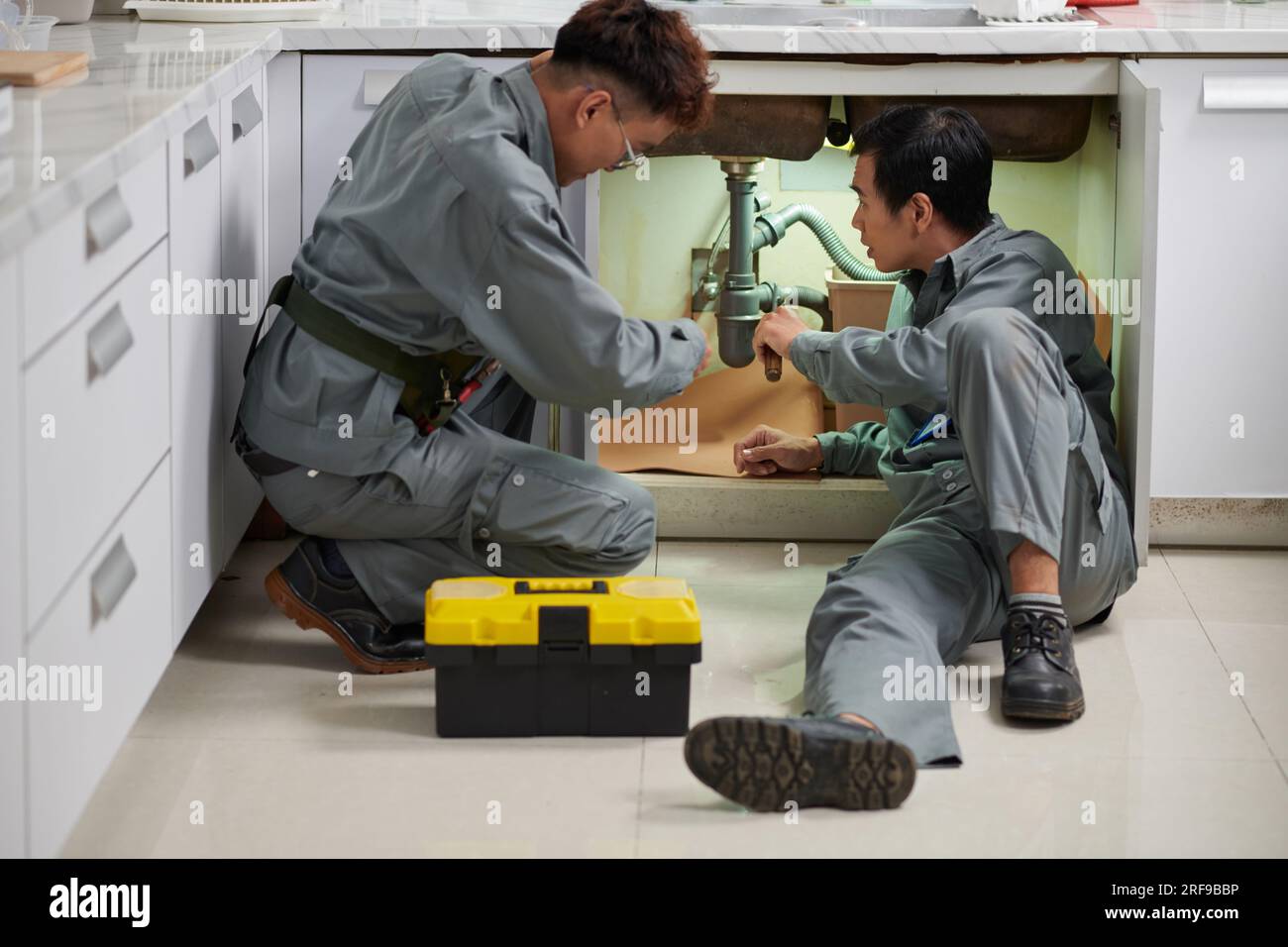 Plumbers installing new plastic pipes under kitchen sink Stock Photo