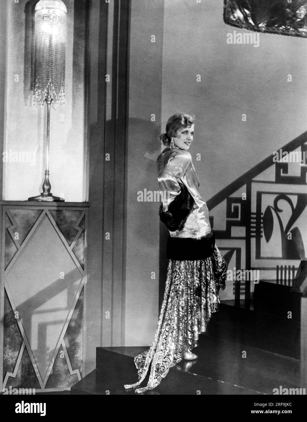 Hollywood, California:  c. 1929 Russian movie star Olga Baclanova models an evening gown made of gold cloth, sequins, crystals, and a gold lace. She is wearing it with a gold finger-tip length coat bordered with brown sable fur. Stock Photo